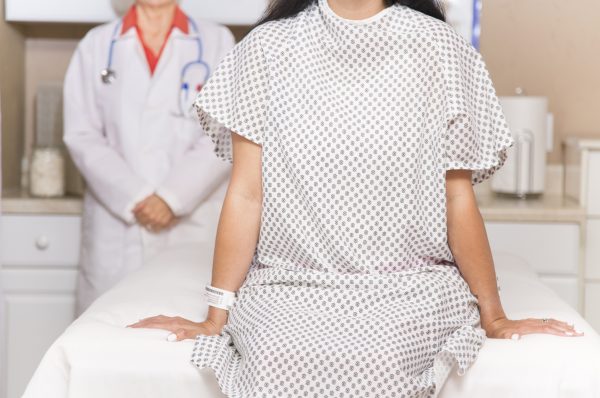 woman wearing hospital gown prepares for medical procedure. her doctos is behind her and both are facing the camera