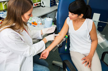 A doctor wearing white gloves prepares to draw blood from her patient's arm