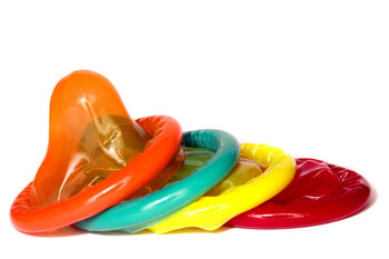 Four rolled up condoms in a row, one orange, one teal, one yellow, and one red