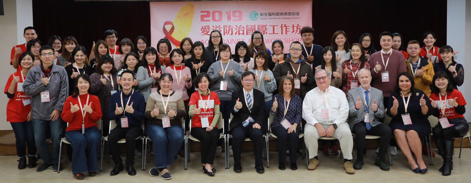 A group of about 50 participants and trainers in the Taiwan training pose for a picture, smiling and making thumbs up