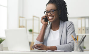 Contact tracer (woman in a white shirt and grey jacket) makes a phone call on a mobile phone, and is taking notes on a laptop