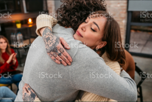Person with tattoos embracing another person with eyes closed