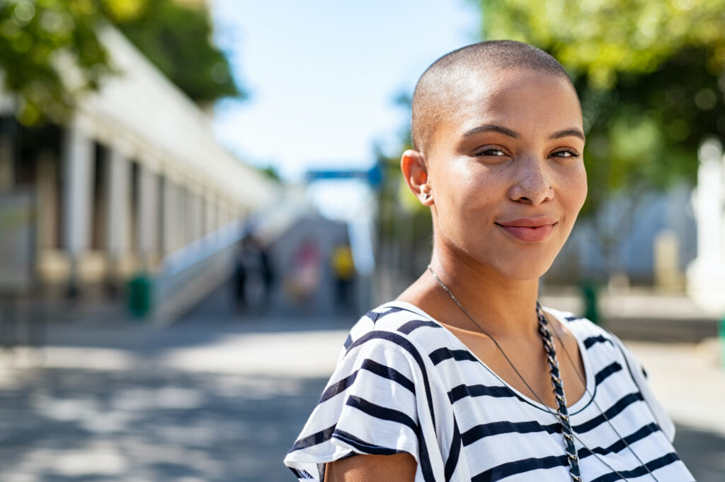 Portrait of young happy bald woman on city street looking at camera. 