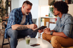 Two men sitting at a table conversing over an iPad