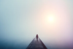 Woman crossing the bridge over lake on a foggy winter day.