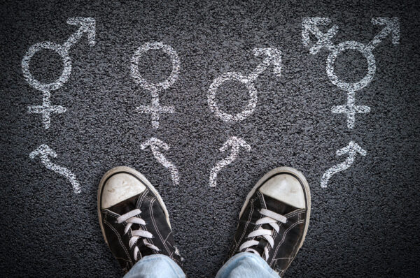 A person standing on asphalt road with male, female, bigender and transgender gender symbols.
